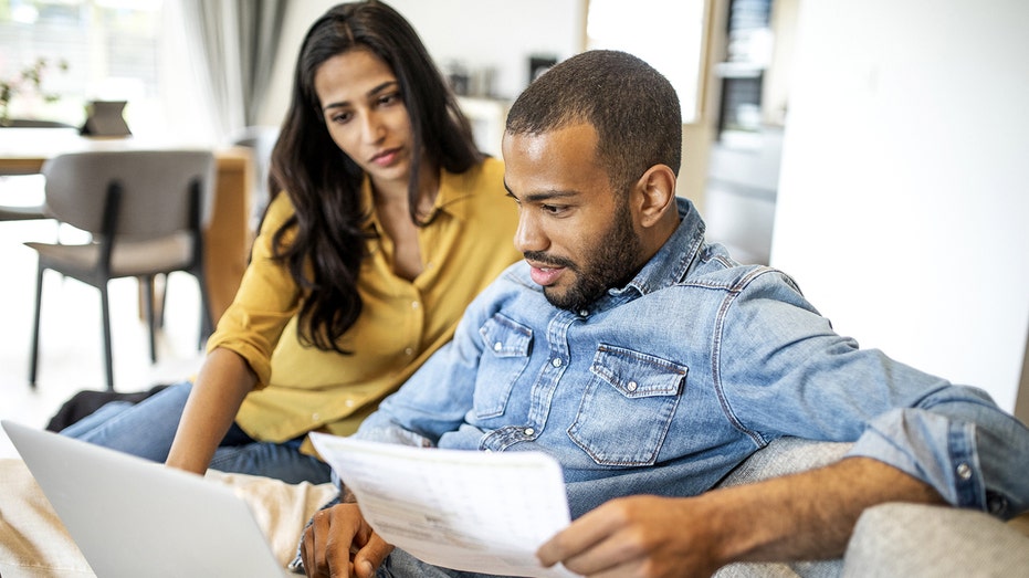 Man and woman review paperwork on a couch at home.